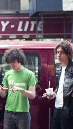 three young men standing in front of a red van looking at their cell phones and drinking coffee