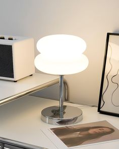 a white table lamp sitting on top of a desk next to a framed photo and radio