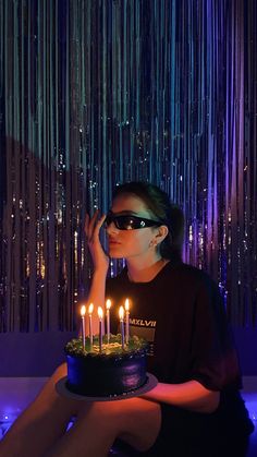 a woman sitting in front of a cake with lit candles on it and wearing sunglasses