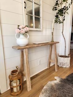 a wooden table topped with a white vase filled with flowers next to a mirror and potted plant