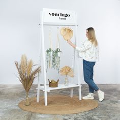 a woman standing next to a white shelf with plants on it