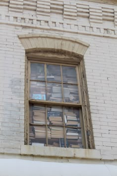 an old window with books in it on the side of a white brick building,