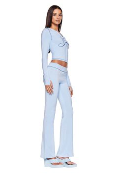 A woman stands posing in a light blue I.AM.GIA BLARE TRACKPANT - BLUE: BABY BLUE outfit consisting of a long-sleeve crop top with lace-up detail and matching flared pants. She pairs the ensemble with light blue platform sandals and has straight, dark brown hair. The background is plain white. Matching Set Women’s, Areopostle Clothes, Blue Kawaii Clothes, Cyan Clothes, Y2k Loungewear, Track Suits Women Style, Cute Sets Two Pieces, Blue Set Outfit, Iam Gia