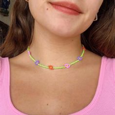 a close up of a woman wearing a pink shirt and green necklace with flowers on it