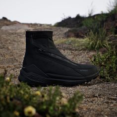 a pair of black shoes sitting on top of a gravel road next to plants and bushes