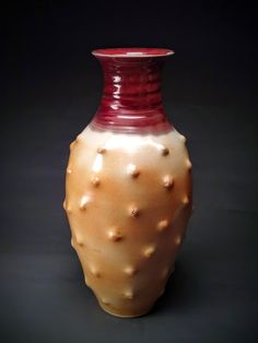 a red and white ceramic vase sitting on top of a table next to a black background