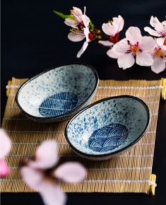 two blue and white bowls sitting on top of a bamboo mat next to pink flowers