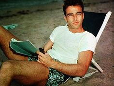 a man sitting on top of a beach chair next to the ocean holding a book