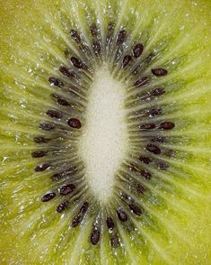 a kiwi fruit sliced in half with water droplets on it's center and seeds