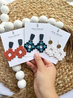 three pairs of earrings on top of a table next to eggs and straw hat with white beads