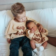 two young children are sitting on a white couch and one is holding the baby's head