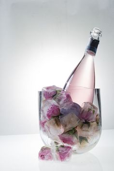 a glass filled with ice and pink flowers next to a bottle of wine on top of a table