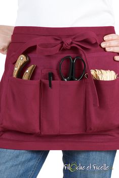 a woman wearing a red apron with scissors and other items in her pocket on her waist