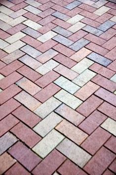 a red brick sidewalk with white and gray bricks on it's sides, next to a bench