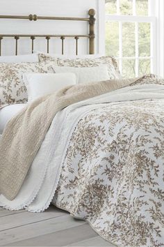 a bed with white and brown comforters in a bedroom next to a window,