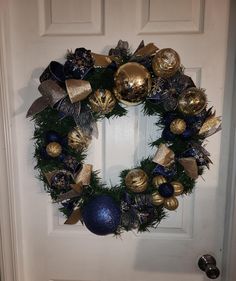 a christmas wreath with gold and blue ornaments hanging on the front door to welcome guests