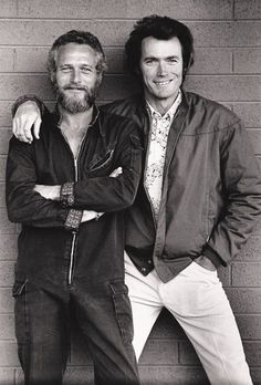 two men standing next to each other in front of a brick wall