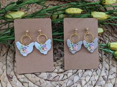 two pairs of butterfly shaped earrings on top of a woven basket next to yellow flowers