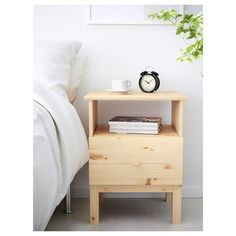 a nightstand with a clock on it next to a bed