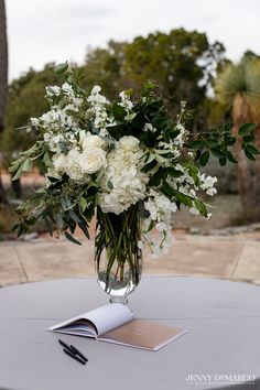 a vase filled with white flowers sitting on top of a table next to an open book