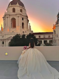 a woman in a wedding dress is sitting on a ledge looking out at the city