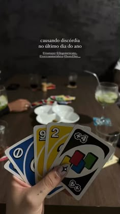 a person holding four cards in front of a table with wine glasses and plates on it