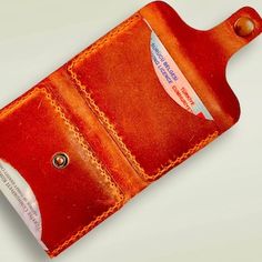 an orange leather wallet with a white tag on the front and red stitching around it