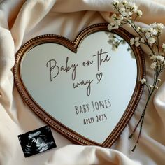 a baby on the way heart shaped mirror with flowers in it and a card attached