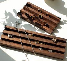 two wooden trays with rings on them sitting next to a cup and necklace holder