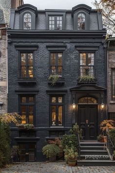 an old black brick building with potted plants on the front and stairs leading up to it