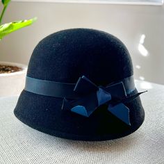 Black Cloche Hat 100% Wool. Its Classic Silhouette Is Accented With A Grosgrain Blue And Black Ribbon Cloche Is French For "Bell." A Cloche Hat Is A Type Of Women's Hat That Features A Distinctive Bell Shape And A Close-Fitting, Short-Brimmed Style - Hence The Name. These Happening Hats Have Been Around For More Than A Century And First Became Popular All The Way Back In The 1920s And '30s, When They Were Primarily Made Of Felt. They Were Also Made Of Beads Or Lace For Evening Wear And In Later Classic Black Mini Hat For Winter, Adjustable Brimmed Black Cloche Hat, Adjustable Black Brimmed Cloche Hat, Black Wool Hat With Short Brim, Black Brimmed Cloche Hat One Size, Black Wool Cloche Hat With Flat Brim, Fitted Black Wool Cloche Hat, Black Brimmed Cloche Hat, Black Cloche Hat With Flat Brim