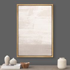 an empty wooden frame hanging on the wall above a table with vases and books