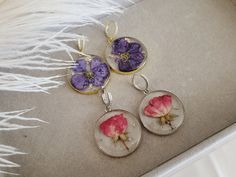 three earrings with flowers in them sitting on a white furnishing area next to a feather