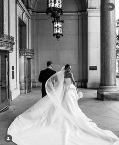 a bride and groom are walking through an old building with columns, chandeliers and windows