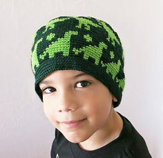 a young boy wearing a green and black knitted hat with an animal design on it