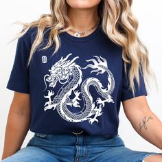 a woman sitting on the ground wearing a blue t - shirt with a white dragon on it