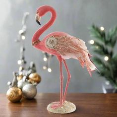 a pink flamingo standing on top of a wooden table next to christmas ornaments and a tree