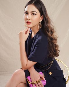 a woman is sitting on a chair with her hand on her chin and wearing gold earrings