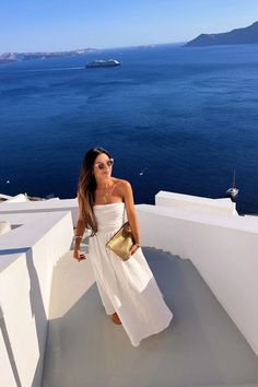 a woman standing on top of a white building next to the ocean with her hand in her pocket