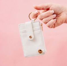 a hand holding a small white purse with two gold rings on it and a pink background