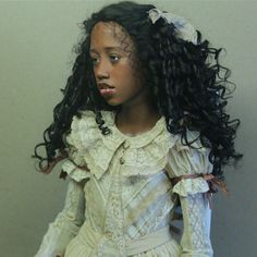 a close up of a doll wearing a dress with long curly hair and laces