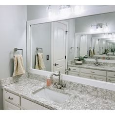 a bathroom with marble counter tops and white cabinets, lights on above the sinks and mirrors