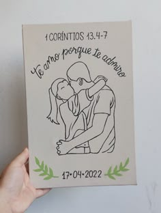 a hand holding up a small canvas with a drawing of a man kissing a woman