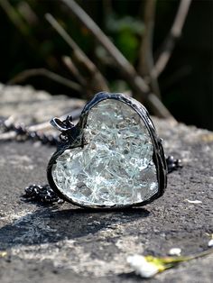 a heart shaped piece of glass sitting on top of a rock