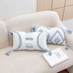 two blue and white pillows sitting on top of a couch next to a book with a price tag