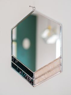 a mirror hanging from the side of a white wall next to a green wall and a light fixture