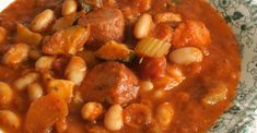 a bowl filled with beans and meat in a tomato based sauce on top of a table