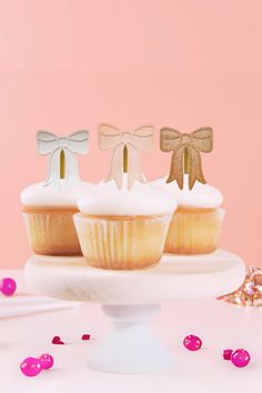 three cupcakes with bows are on a cake plate