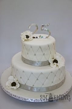 a three tiered wedding cake with white flowers and silver trimmings on top