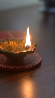 a lit candle sitting on top of a wooden table next to a red plate with an ornate design